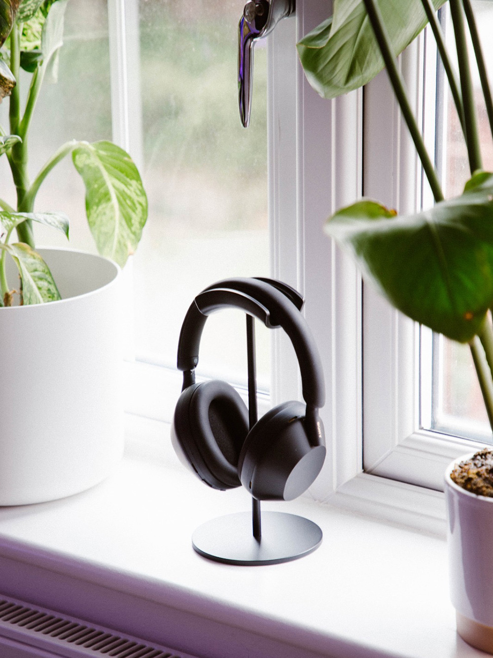 A close-up of the black Sony XM5 headphones on my windowsill, sitting on a stand