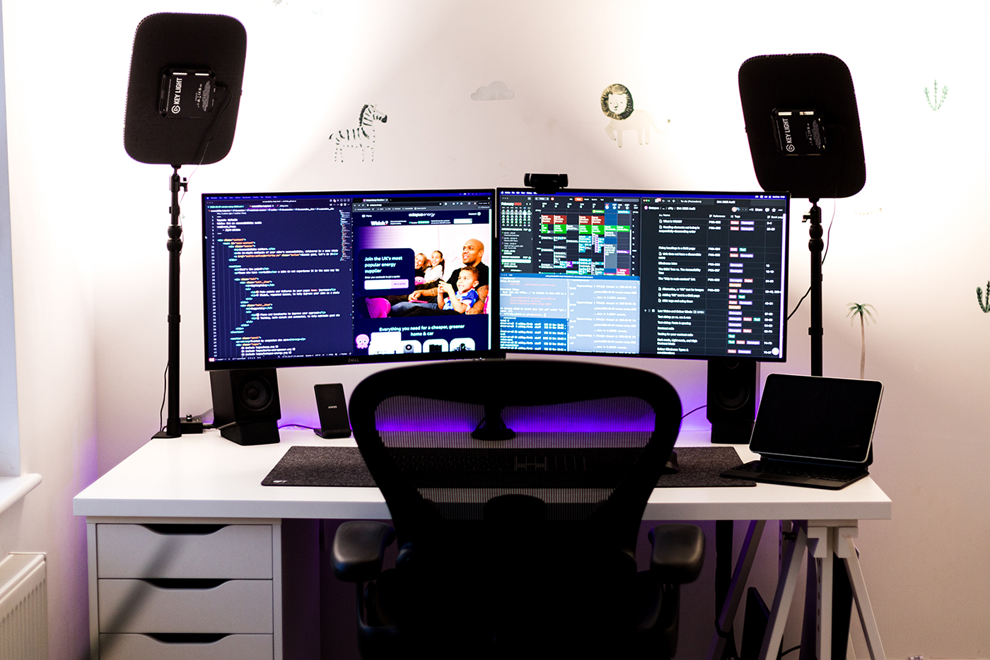 Front on view of a desk with two monitors, speakers and lights each side, white desk and black chair