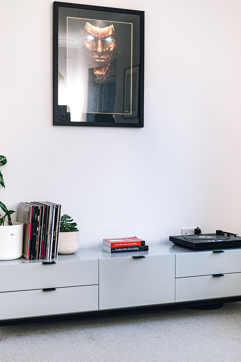 A media unit in my office holds plants, vinyls, and a vinyl player. Above it, a large frame hangs